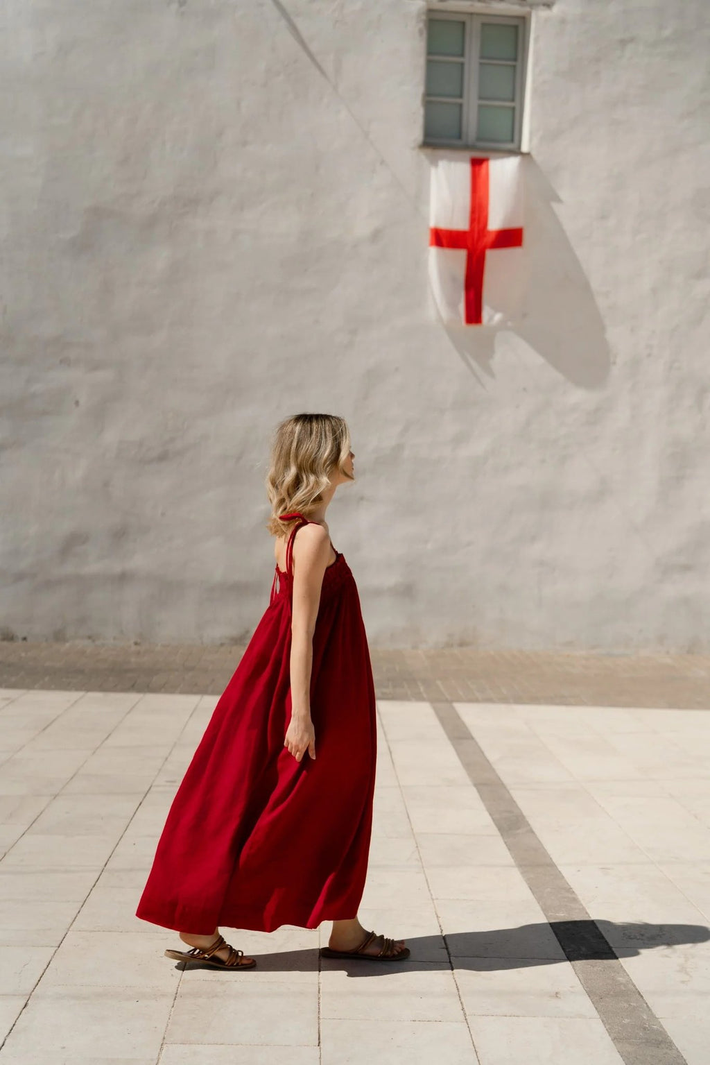3. Woman in red linen Ballade dress walking beside white wall with red cross flag