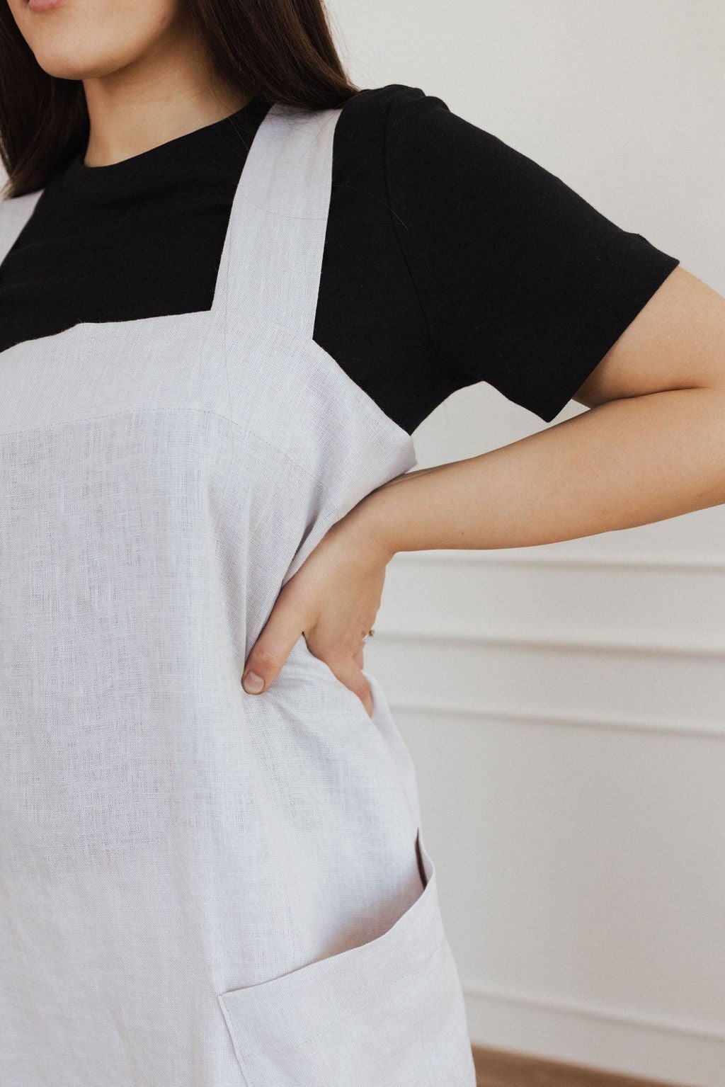 2. Close-up of woman in white linen apron with hand on hip, showing front pocket detail