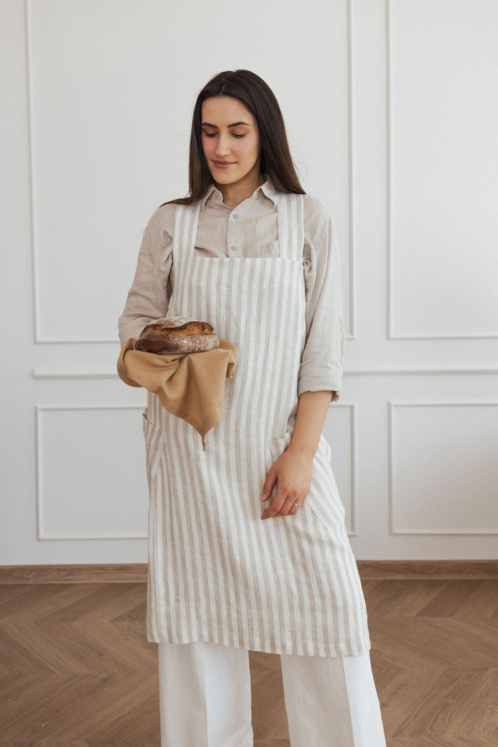 17. Woman in striped linen apron holding bread, standing in a bright room