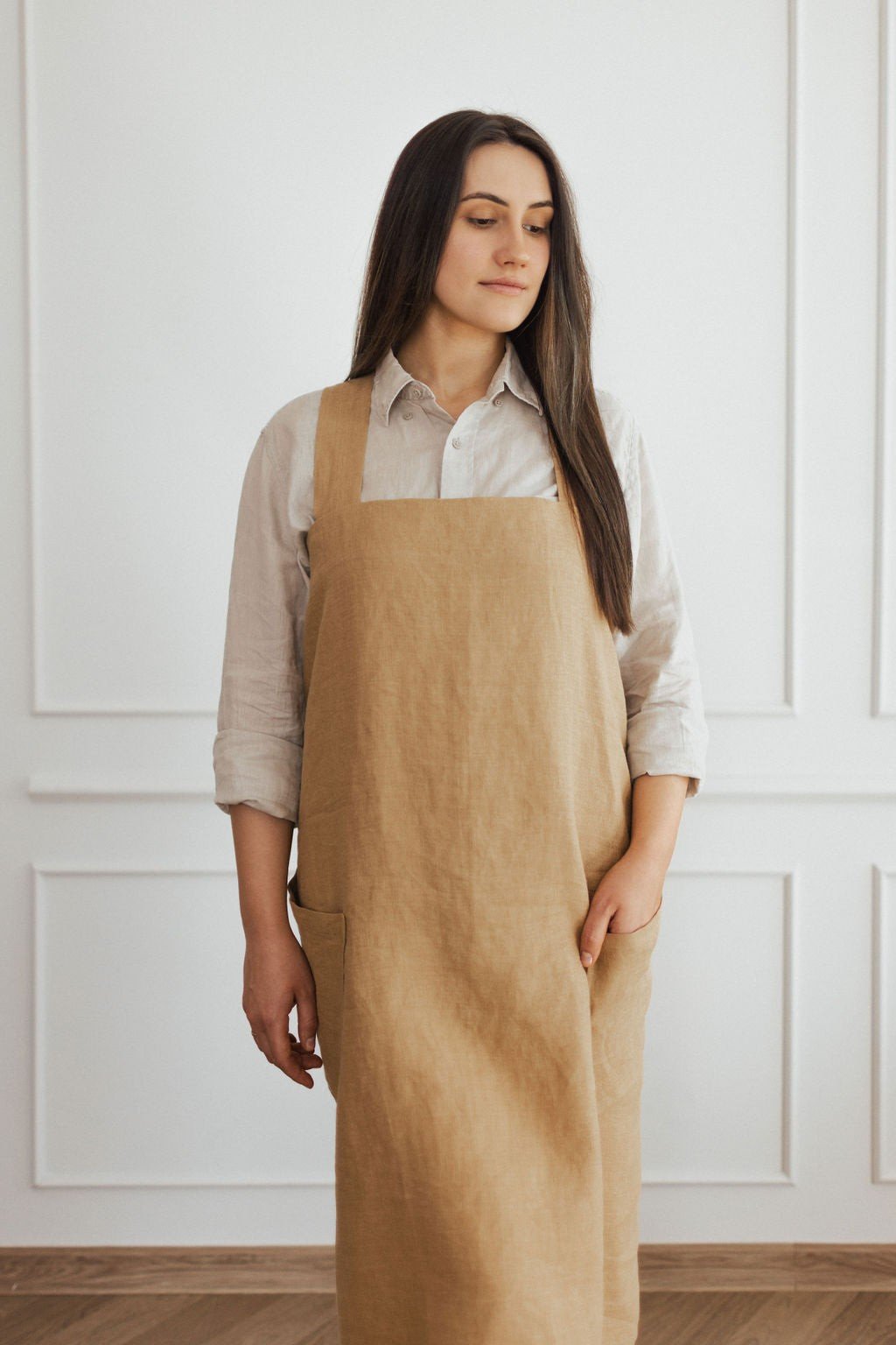 1. Woman wearing beige linen crossed back apron over light shirt in a bright room