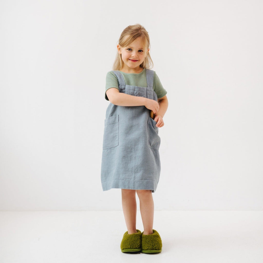 2. Girl in blue fog linen apron with green slippers, arms crossed, in a white studio
