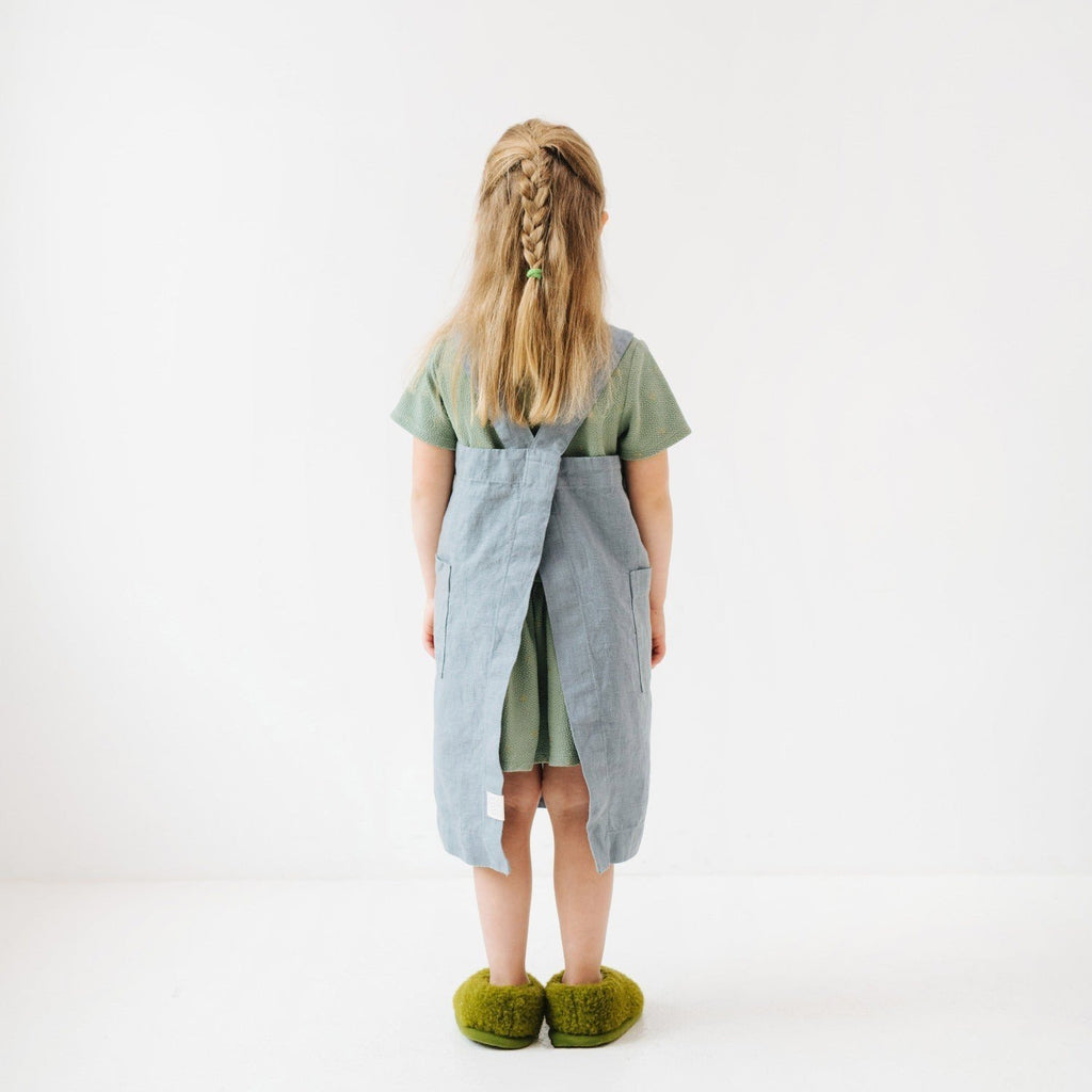 5. Back view of girl in blue fog linen apron with braided hair and green slippers