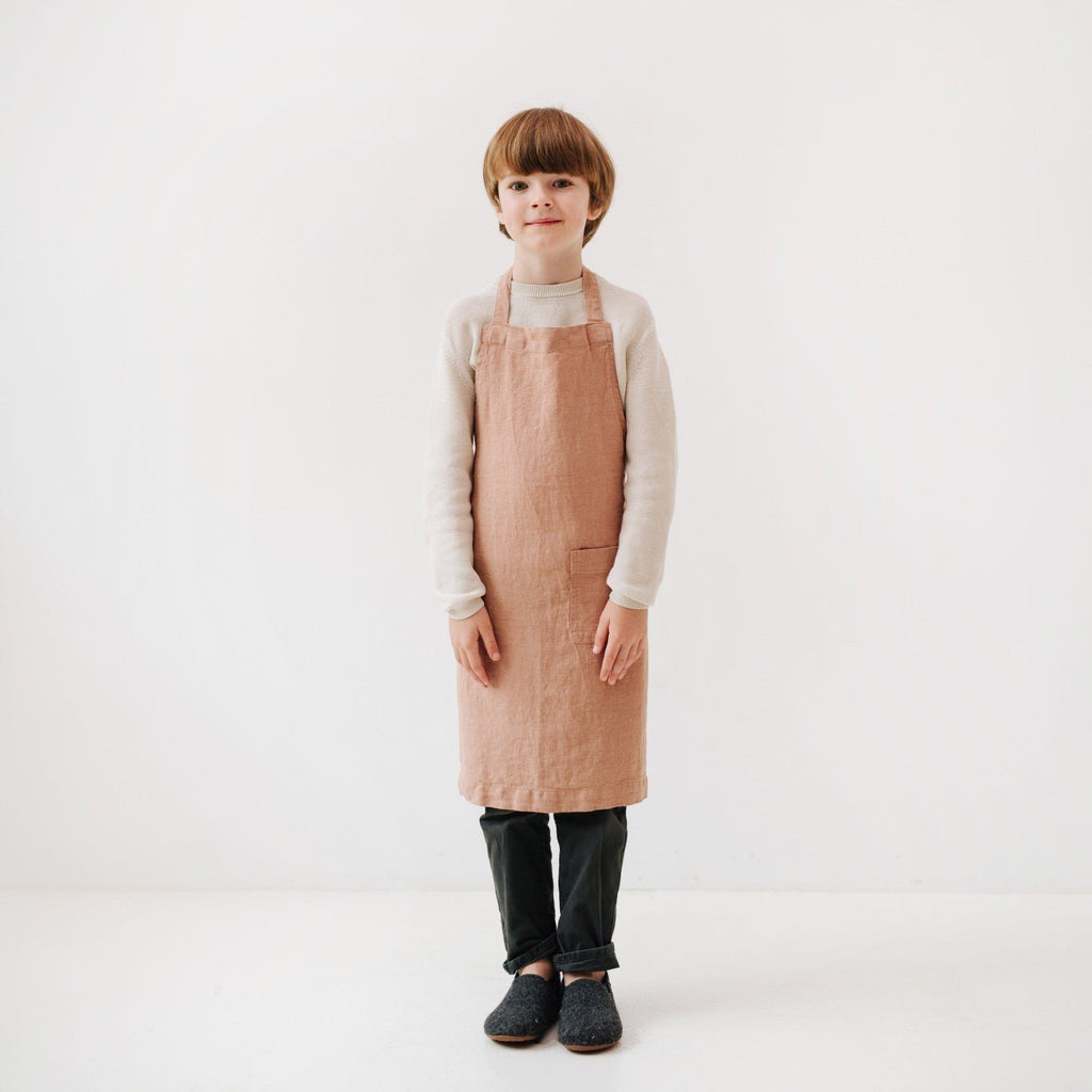 4. Child wearing cafe creme linen apron with hands by sides, studio background