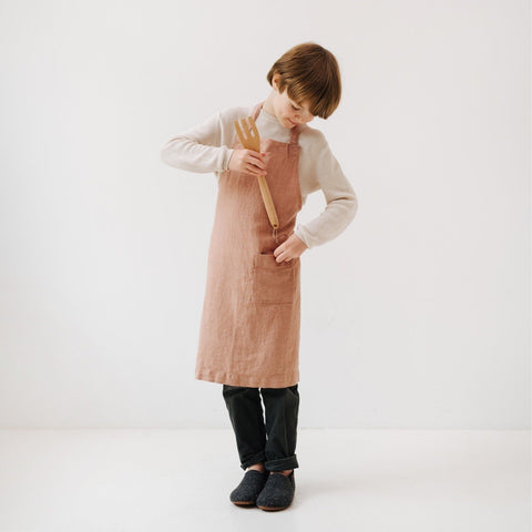 3. Child in cafe creme linen apron placing a wooden fork in front pocket