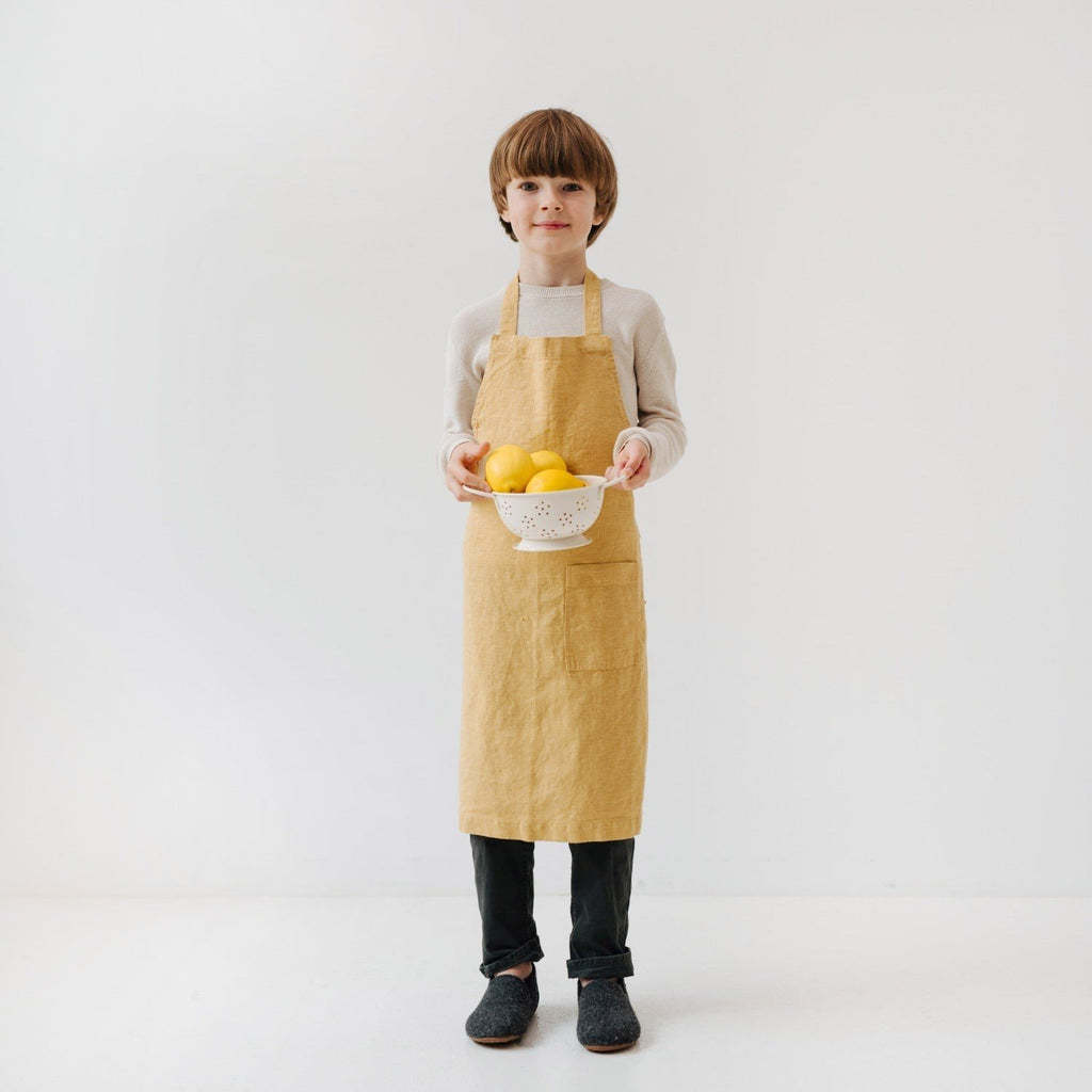 1. Child wearing honey-colored linen apron holding a bowl of lemons in a bright, minimalist setting