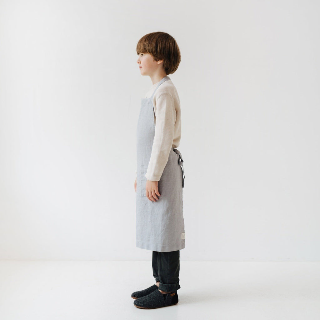 4. Side profile of child in light grey linen apron in a bright setting