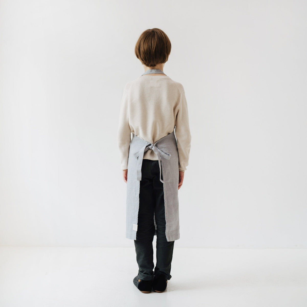 3. Back view of child wearing light grey linen apron with tied closure