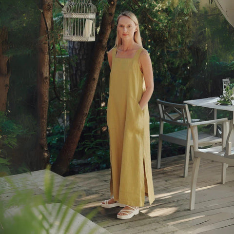 2. Woman in lemon curry linen dress with square neck and pockets, standing on a wooden deck surrounded by greenery