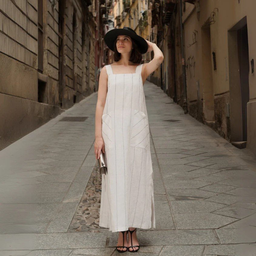 2. Woman in milk white linen dress with grey stripes and black hat standing on cobblestone street