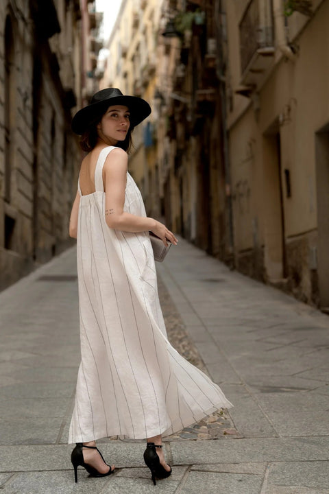 1. Woman wearing milk white linen dress with grey stripes and black hat walking down a narrow street