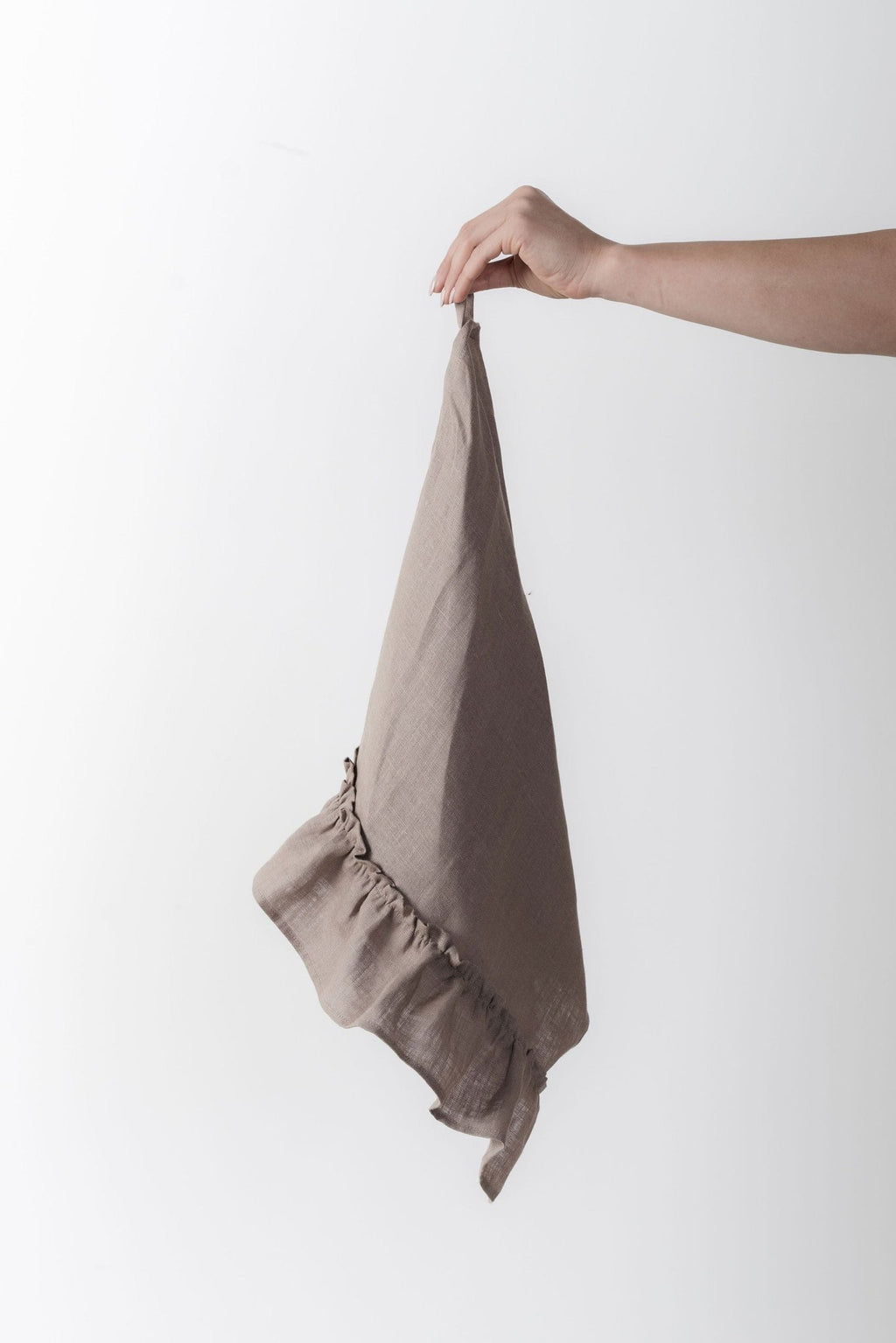 12. Hand holding a cappuccino-colored linen kitchen towel with ruffles against a white background