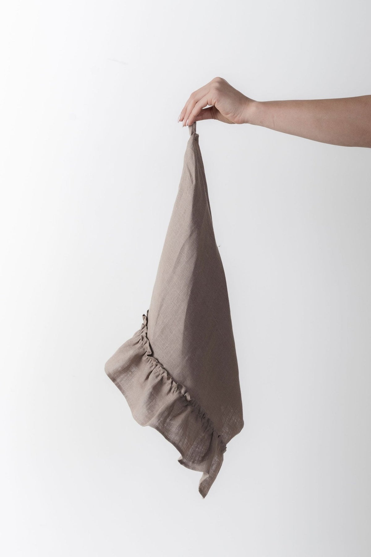 12. Hand holding a cappuccino-colored linen kitchen towel with ruffles against a white background