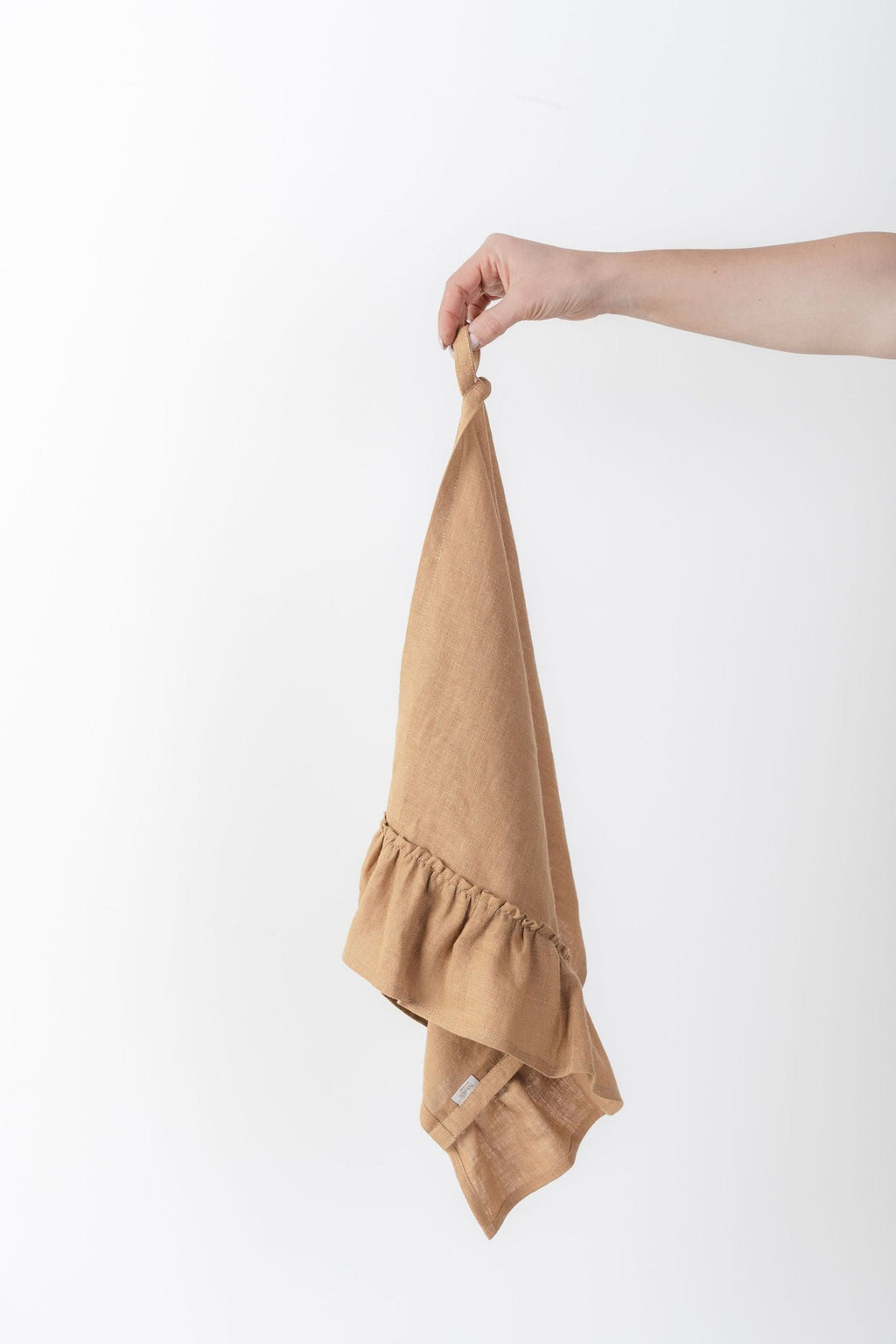 2. Hand holding a caramel-colored linen kitchen towel with ruffles against a white background