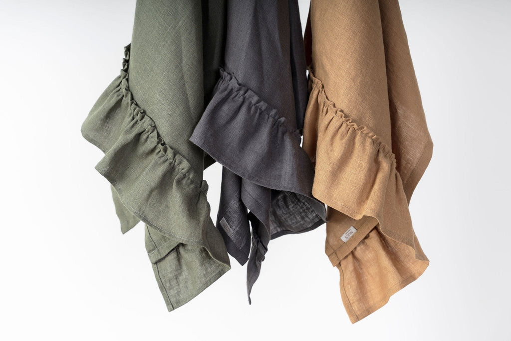 5. Close-up of three linen kitchen towels with ruffles in olive, gray, and caramel hanging on hooks