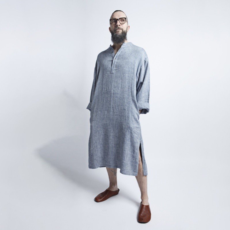 2. Man standing in studio wearing blue-gray linen dress with side slits and brown shoes