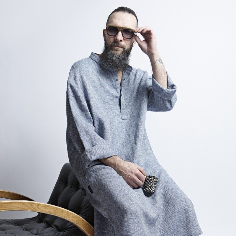 1. Man wearing blue-gray linen dress with big pockets and sunglasses sitting on a modern chair