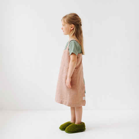 2. Side view of girl in cafe creme linen pinafore apron with green shirt and slippers in a studio