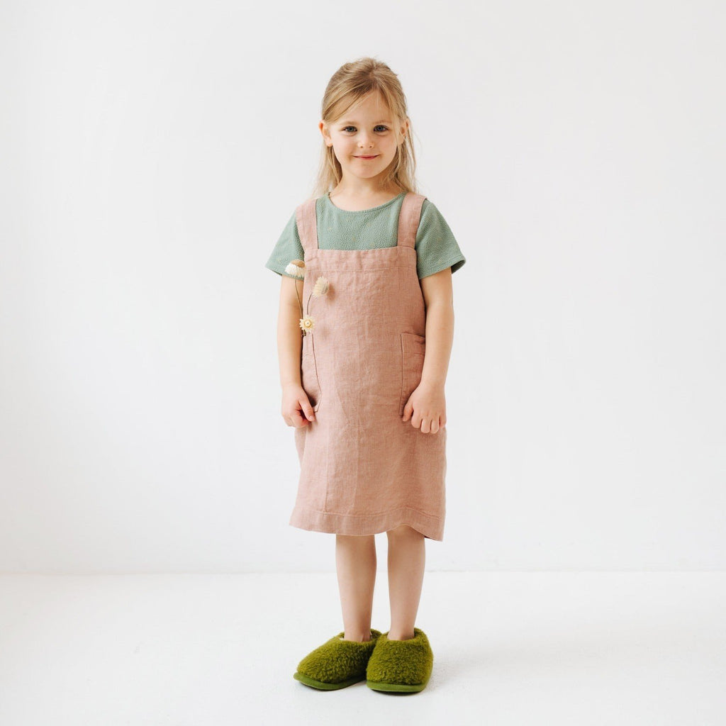 3. Girl in cafe creme linen pinafore apron with green shirt and slippers holding a flower in a studio