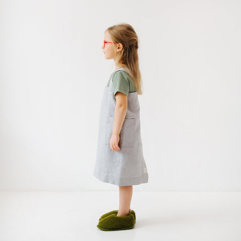 3. Side profile of girl in light grey linen pinafore apron with green top and red glasses