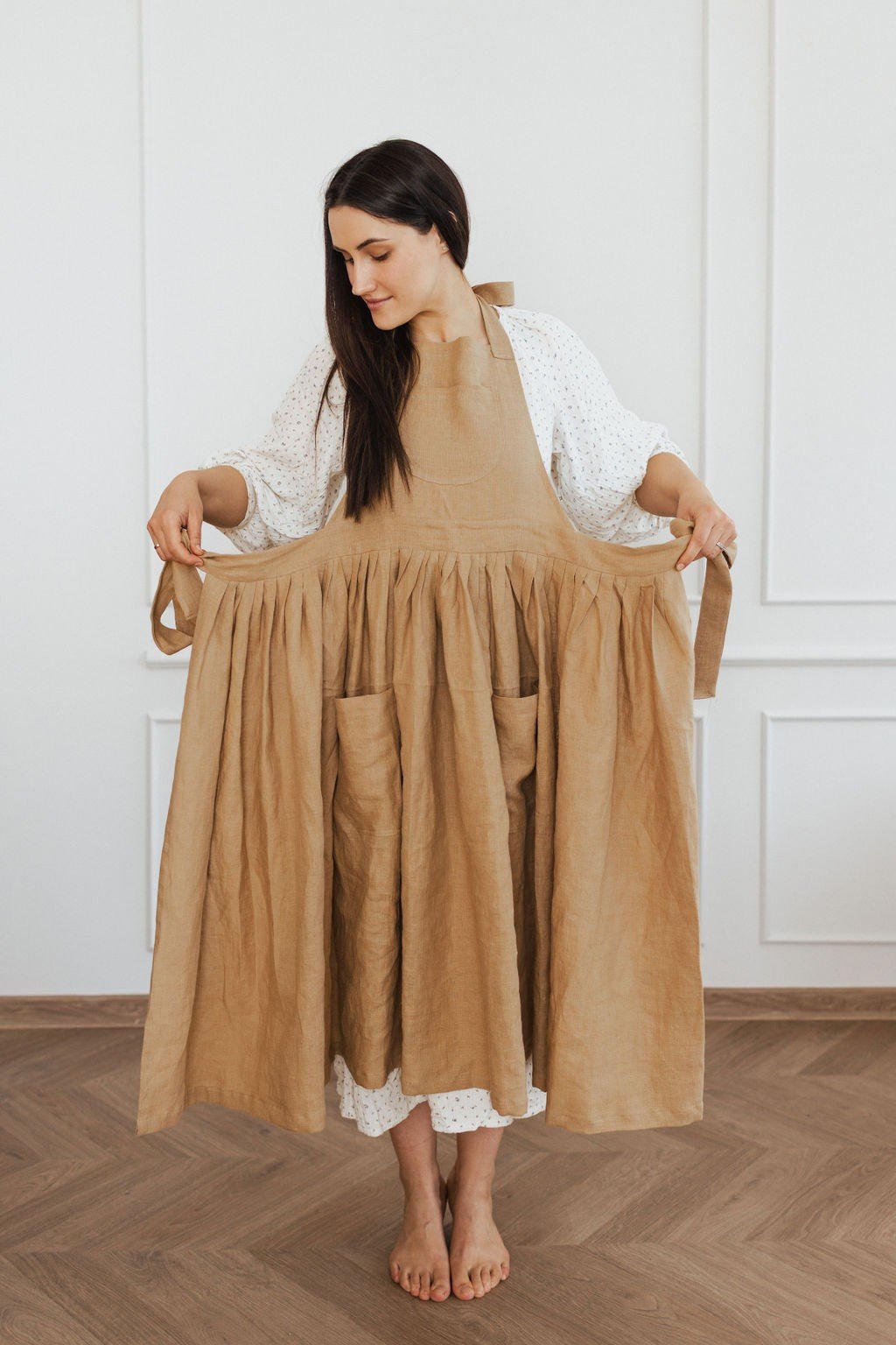 10. Woman holding out brown linen apron in a bright room