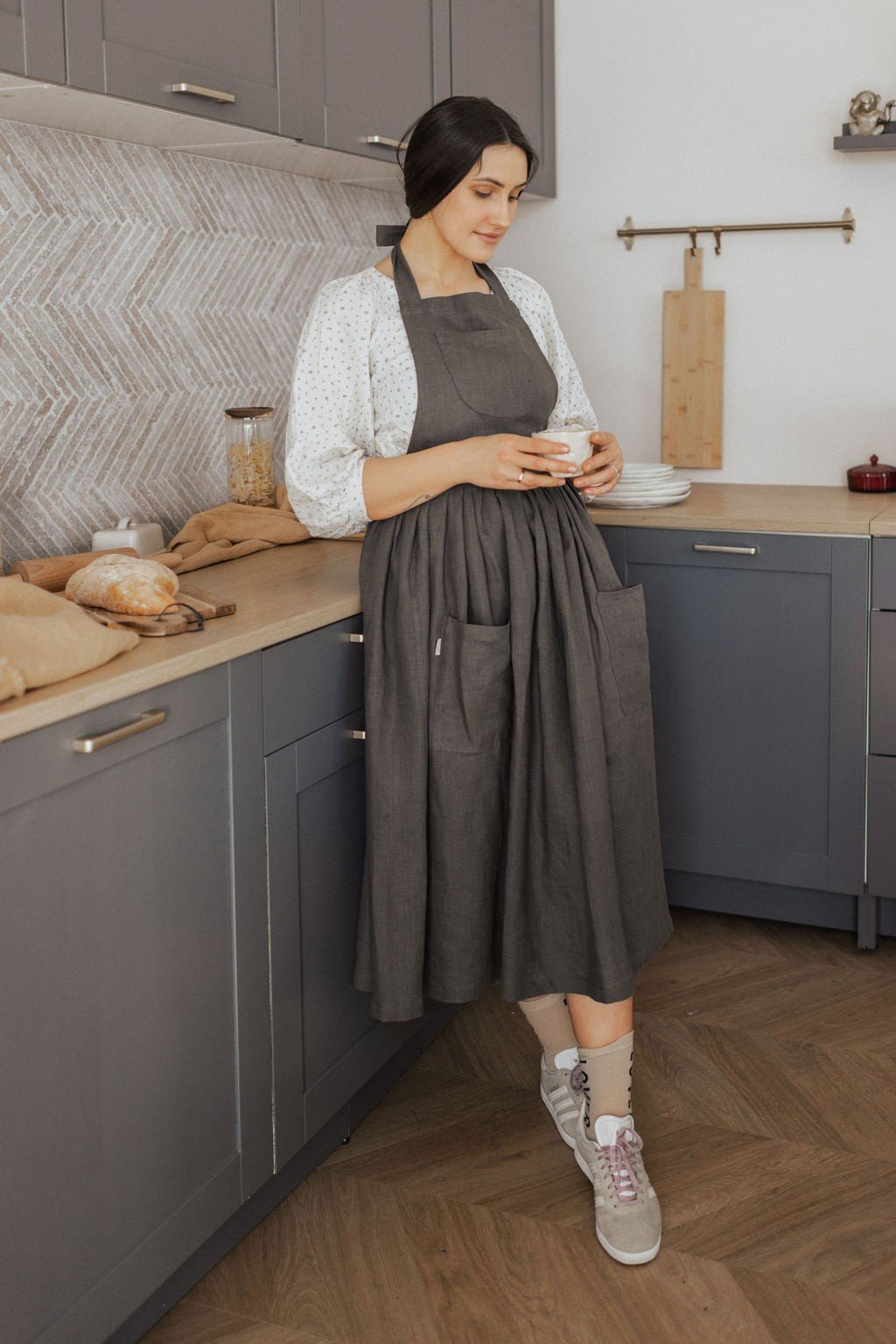 14. Woman in dark grey linen apron holding a cup in a kitchen