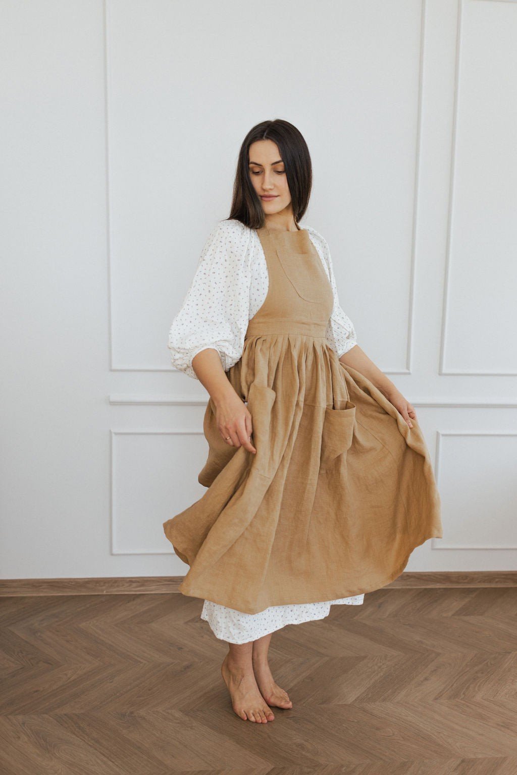 2. Woman twirling in brown linen retro apron with white blouse in a bright room