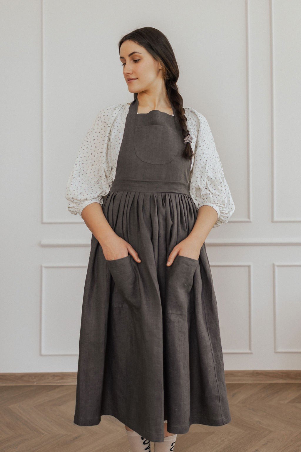 13. Woman in dark grey linen apron with hands in pockets in a bright room