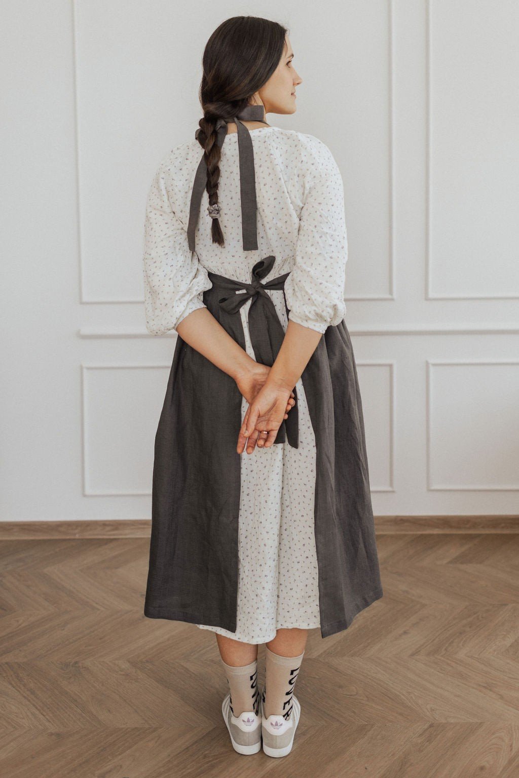 12. Back view of dark grey linen apron tied at the waist over white dress