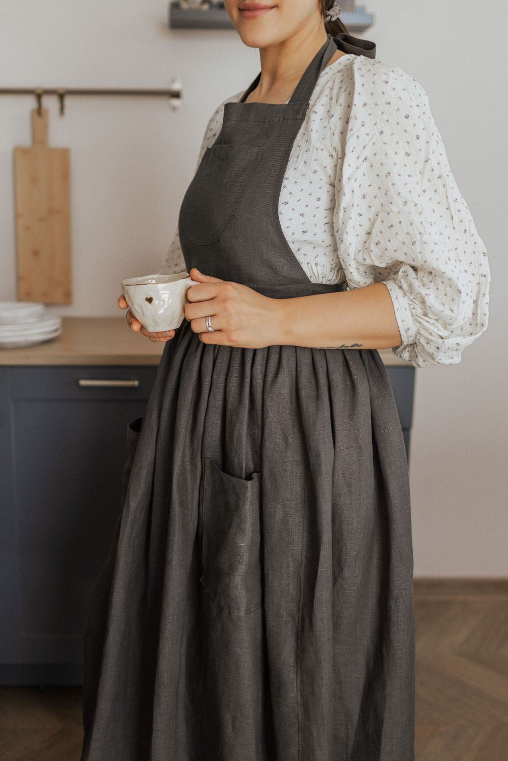 11. Woman in dark grey linen apron holding a cup in a kitchen