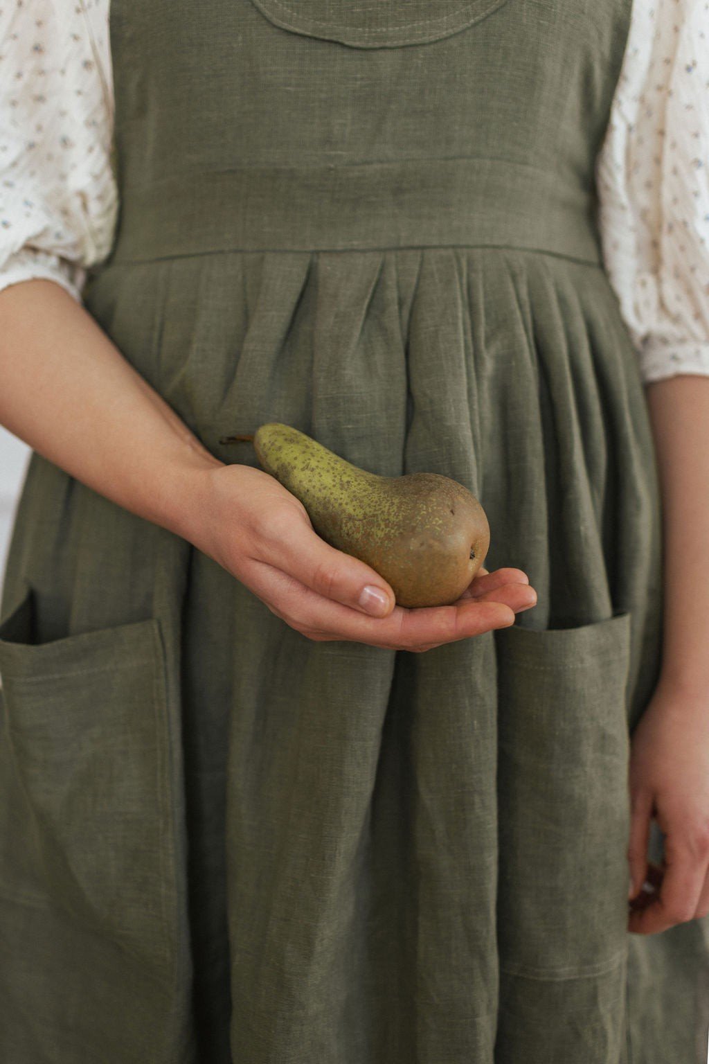4. Close-up of green linen apron with pocket holding a pear