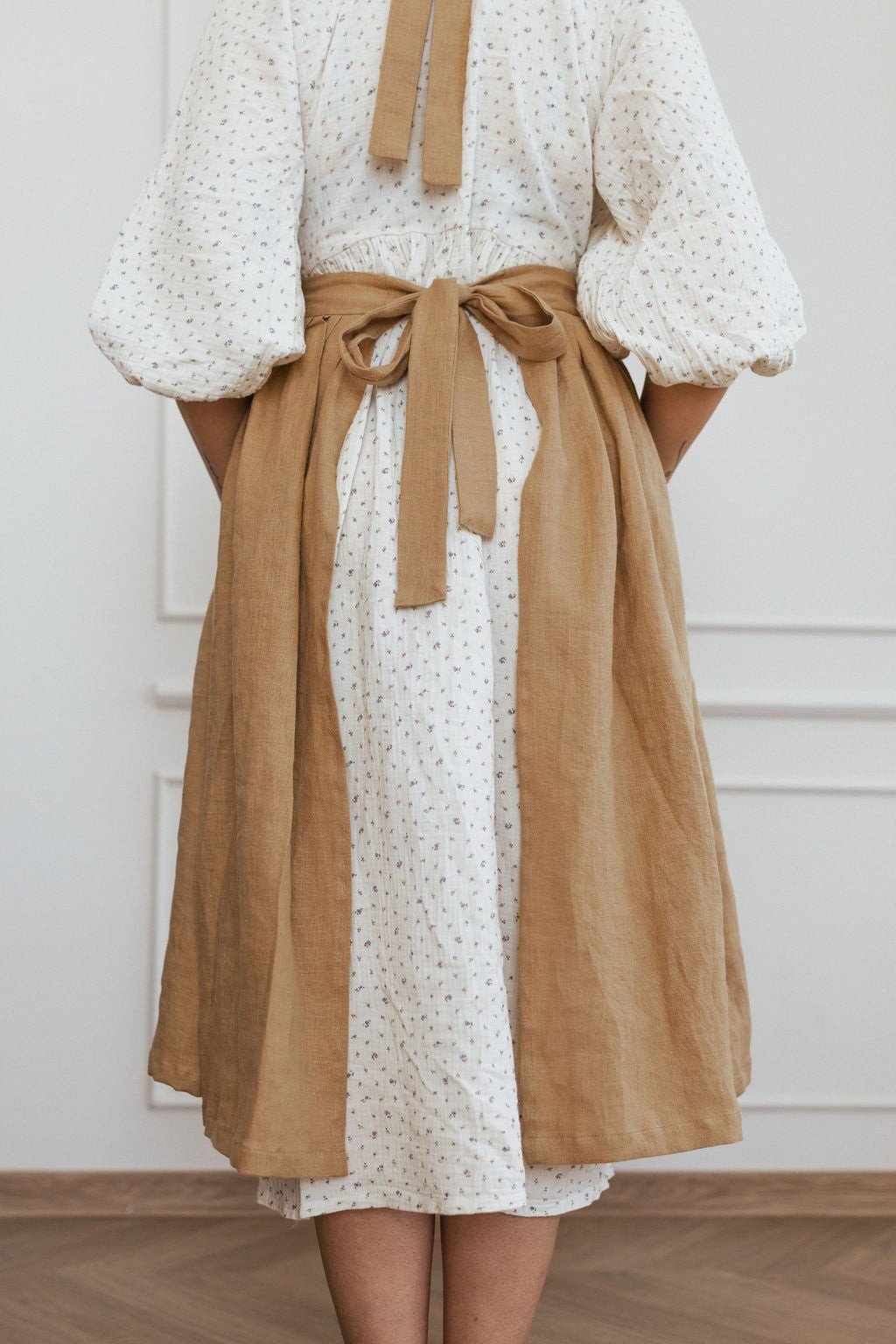 9. Rear view of brown linen apron tied at the waist over white dress