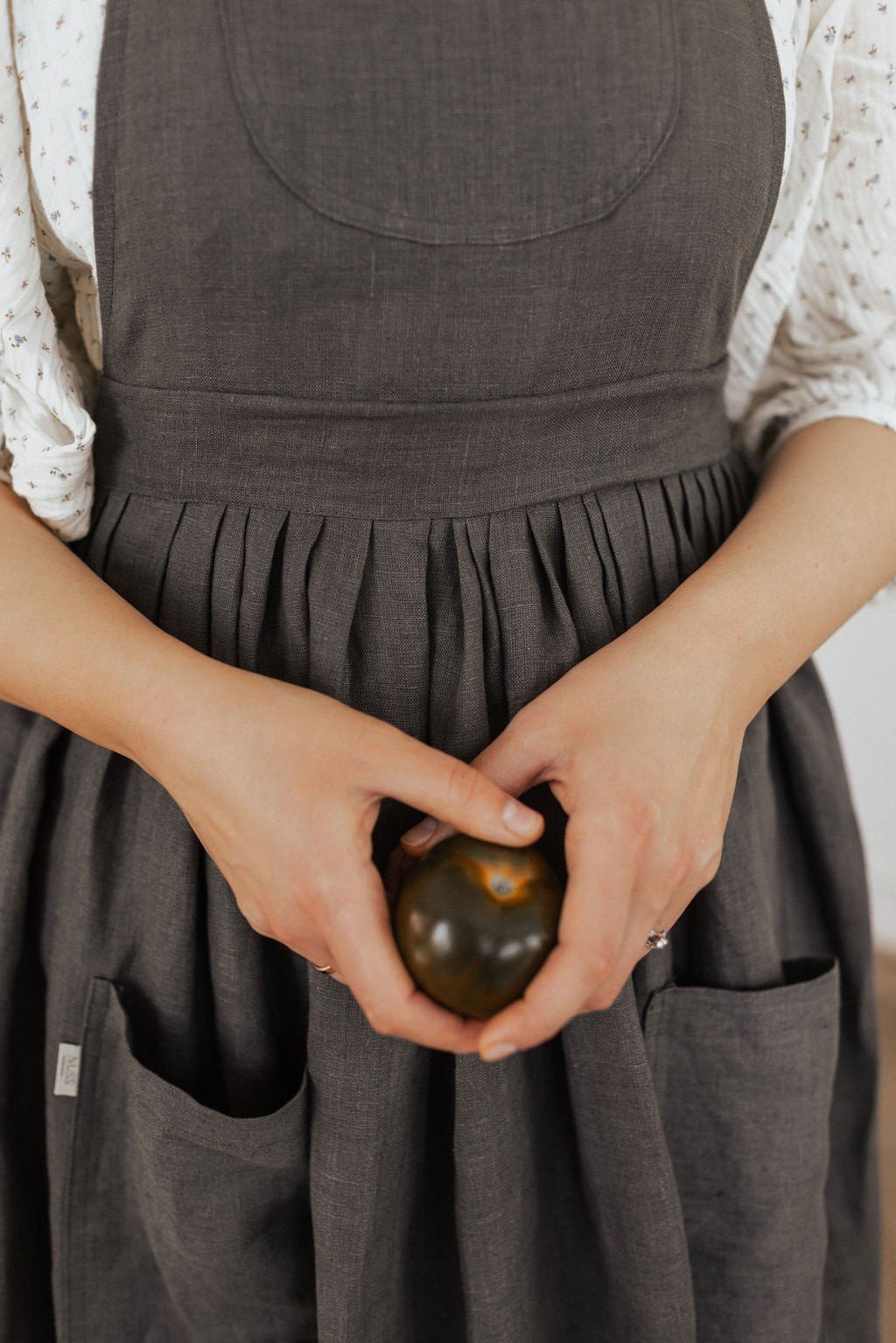 15. Close-up of dark grey linen apron with hands holding an apple