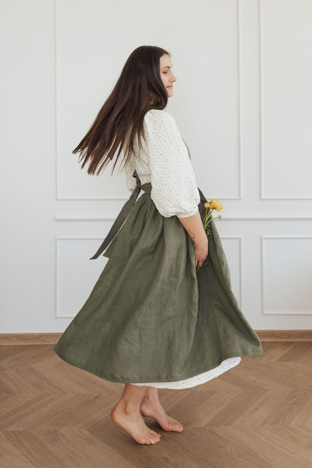 19. Woman twirling in green linen apron with flowers in a bright room