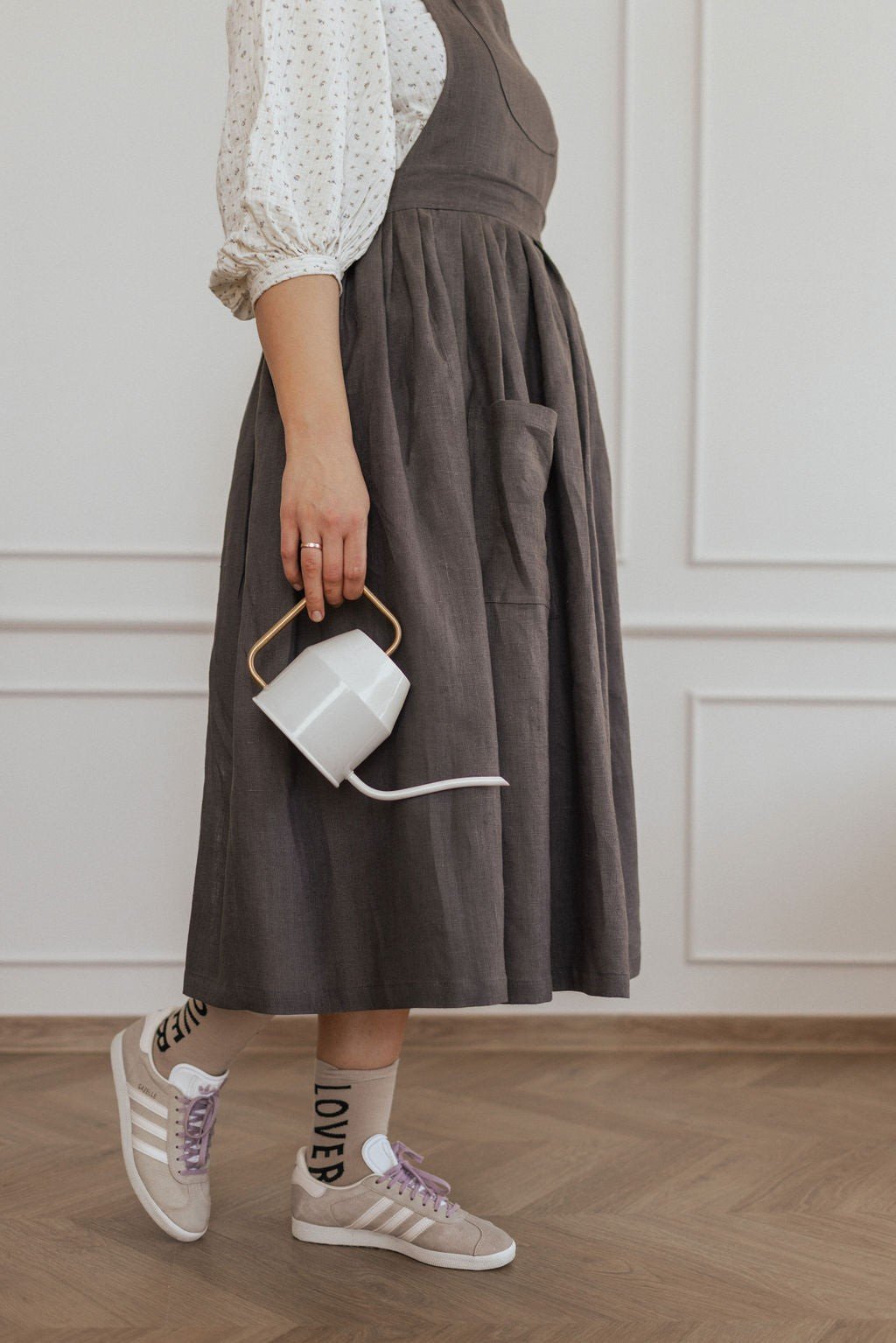 20. Side view of dark grey linen apron with white sneakers and holding a cup