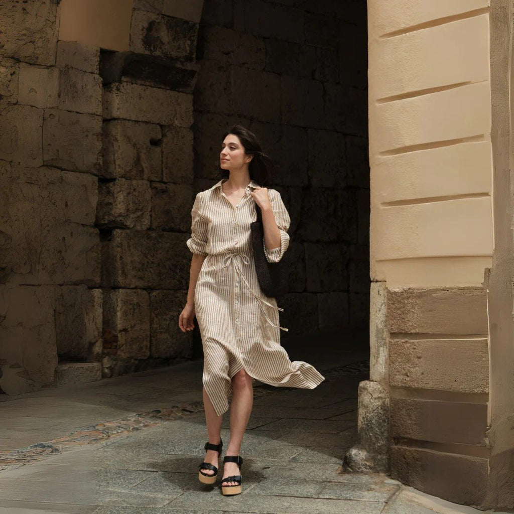 2. Woman in bronze and white striped linen dress with button closure and belt, walking through an archway