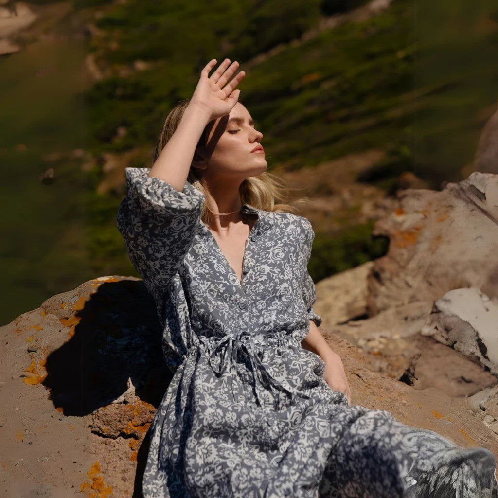 3. Close-up of woman in blue floral linen dress sitting on rock, showing elasticated cuffs and drawstring belt