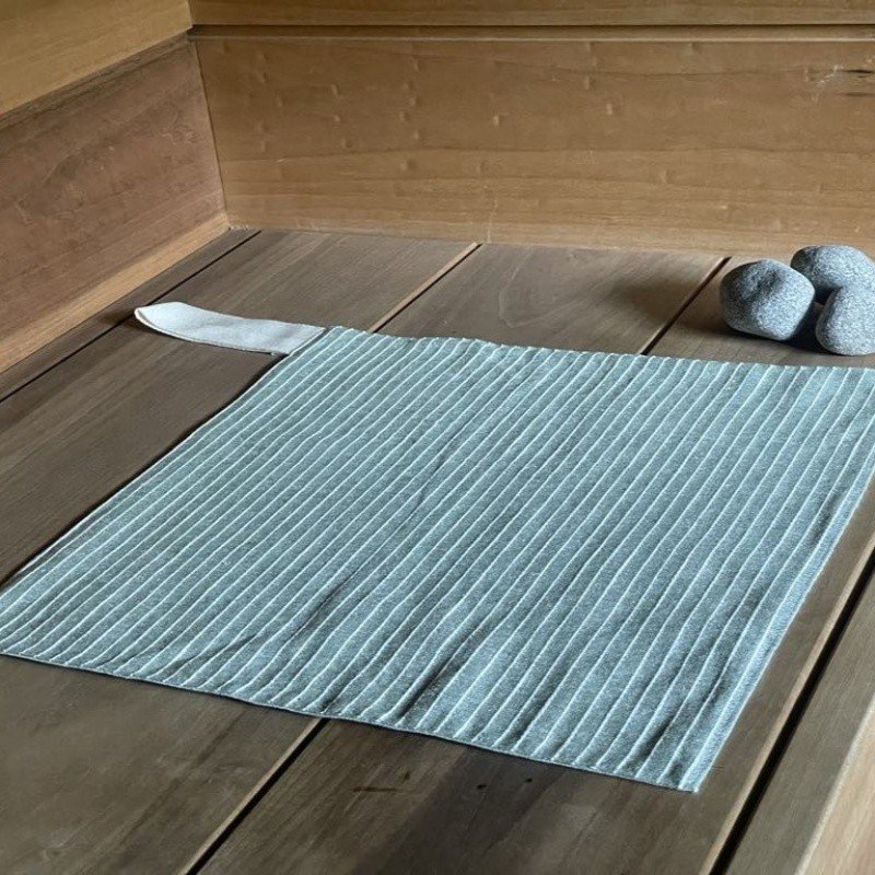 6. Single linen sauna seat cover with light stripes placed on wooden sauna platform, featuring cotton hook and soft texture.