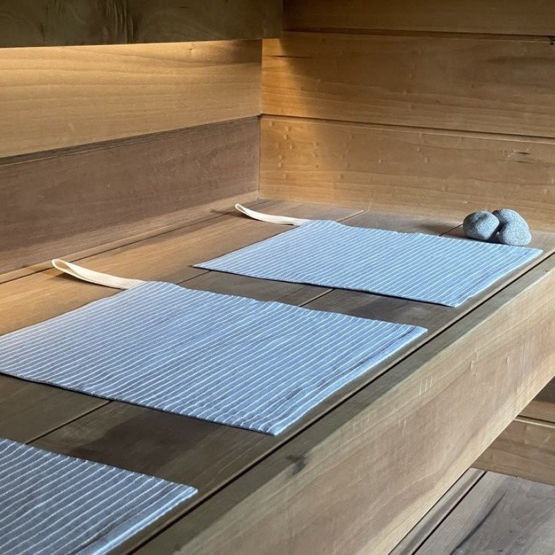 1. Linen sauna seat covers with light stripes placed on wooden sauna platform, showcasing double-sided design and cotton hooks.