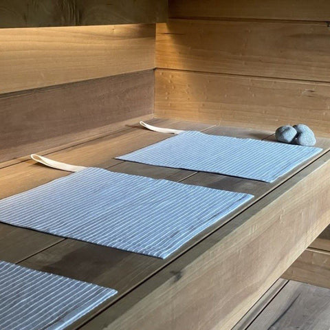 1. Linen sauna seat covers with light stripes placed on wooden sauna platform, showcasing double-sided design and cotton hooks.