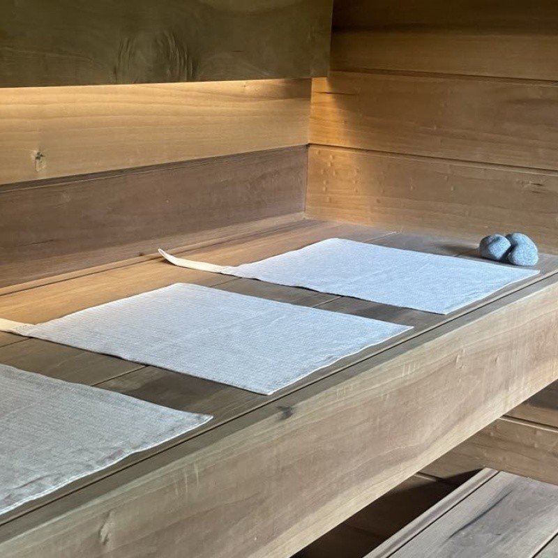 13. Linen sauna seat covers with light stripes placed on wooden sauna platform, showcasing double-sided design and cotton hooks.