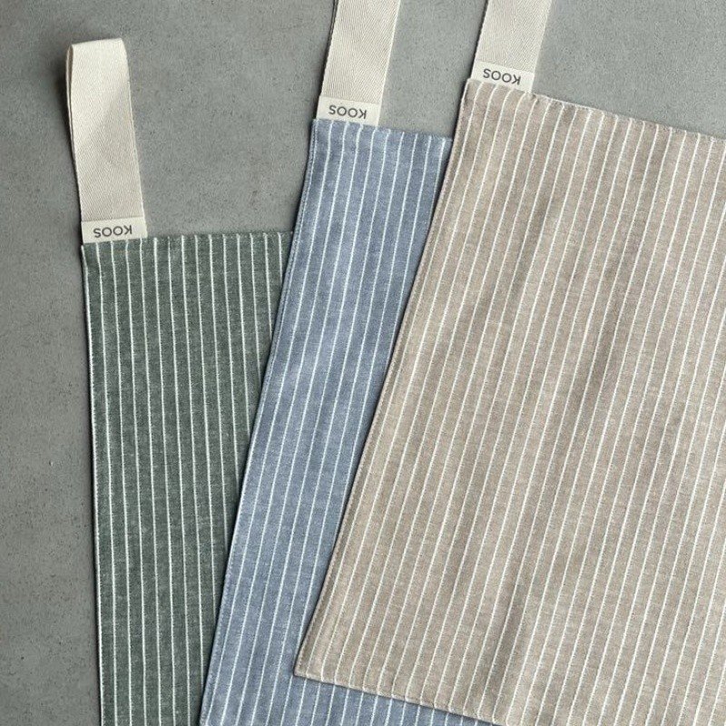 7. Flat lay of three linen sauna seat covers in assorted colors with light stripes and cotton hooks, highlighting brand logo.