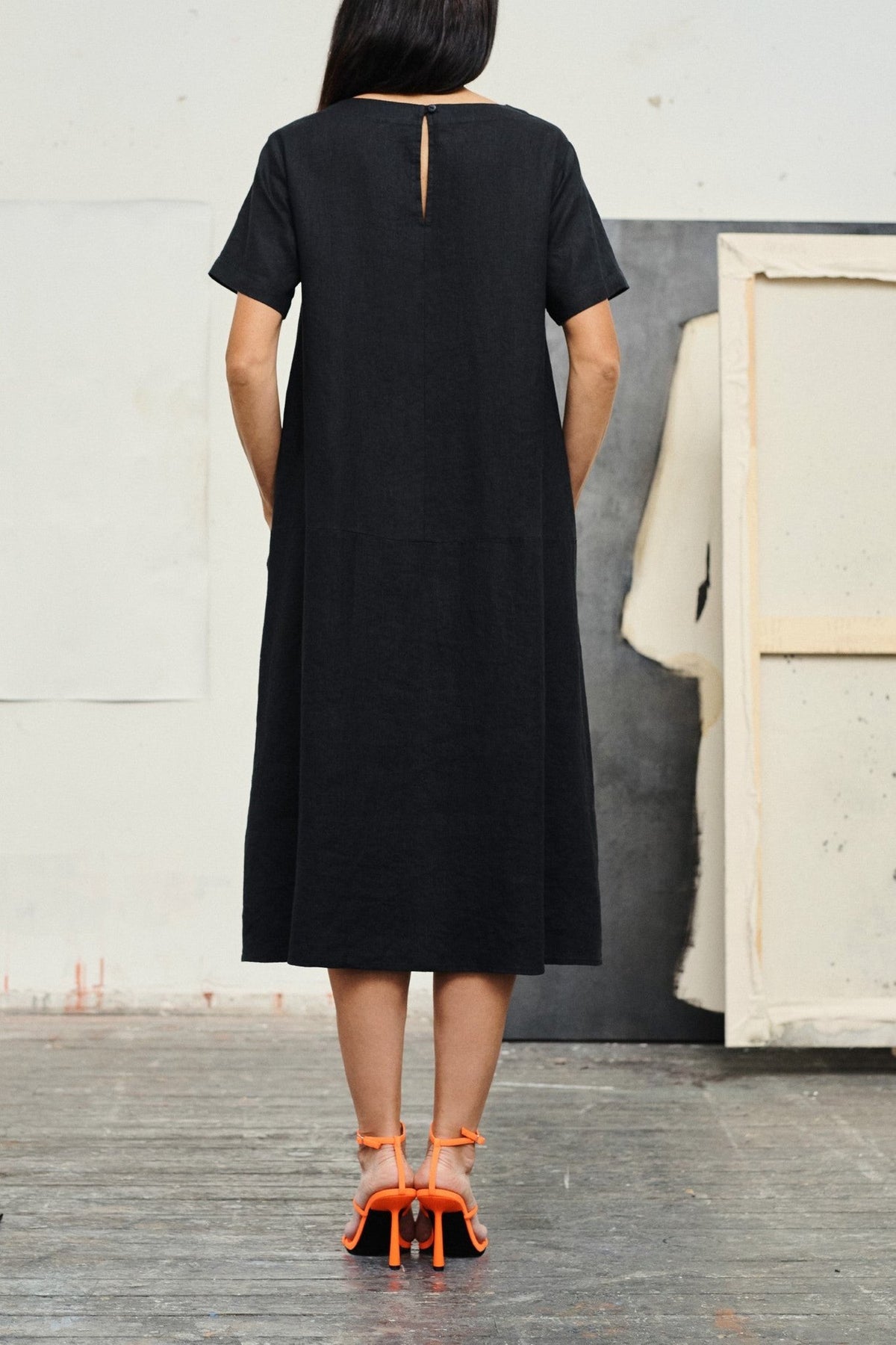 2. Back view of black linen dress with button closure, worn by woman with orange heels