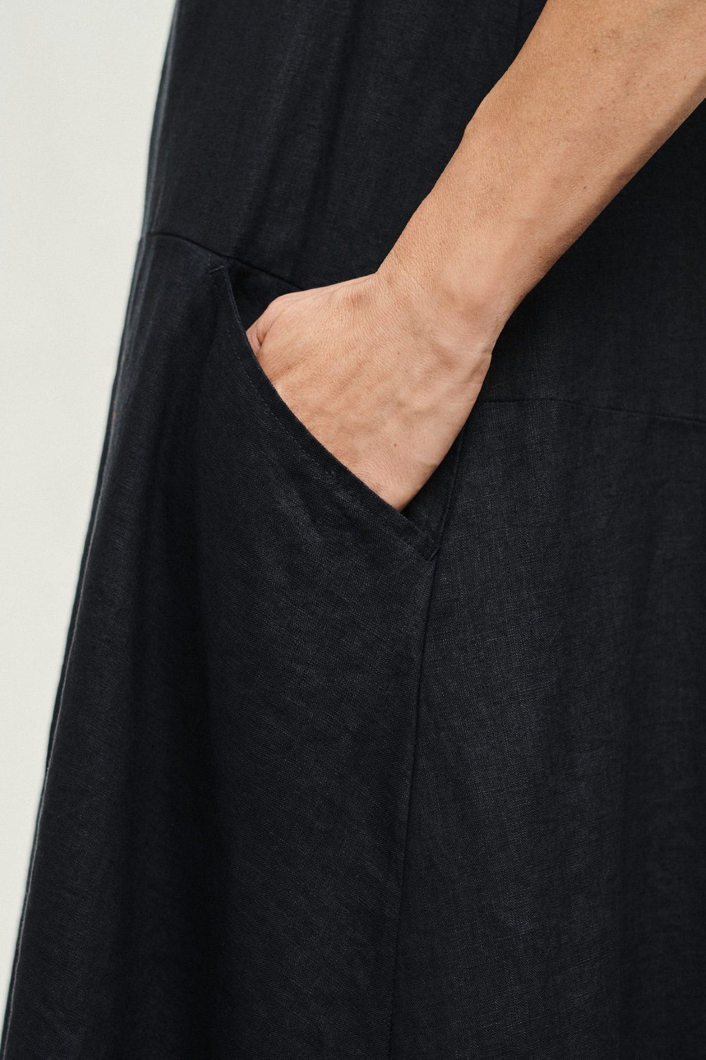 3. Close-up of hand in front pocket of black linen dress showing fabric texture