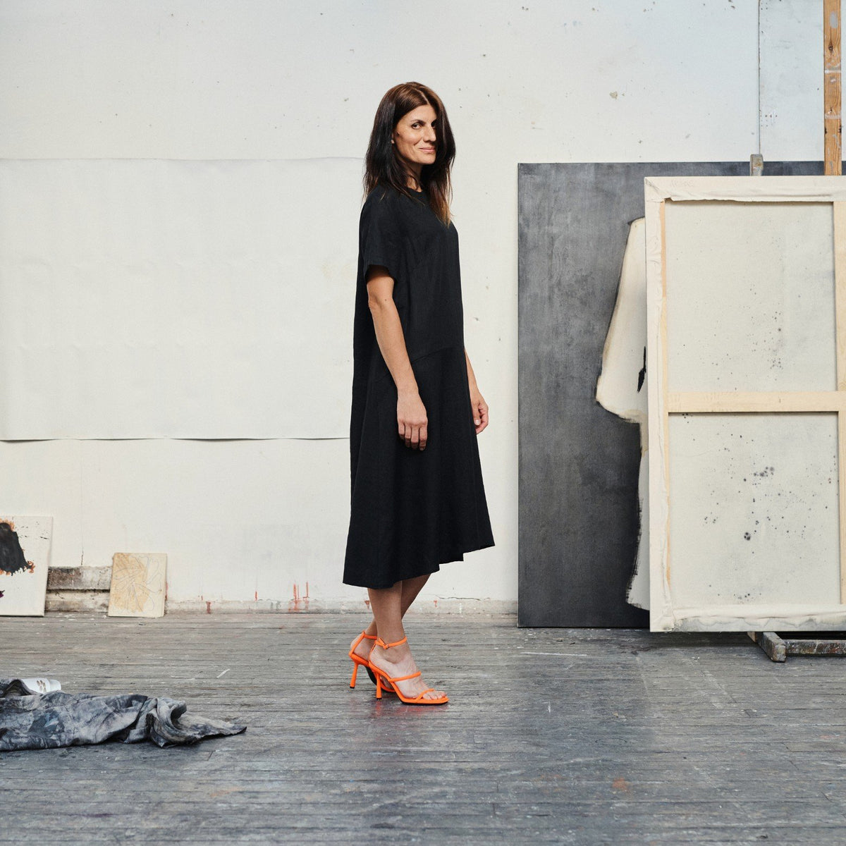 1. Woman wearing black linen A-line dress with orange heels in an art studio setting