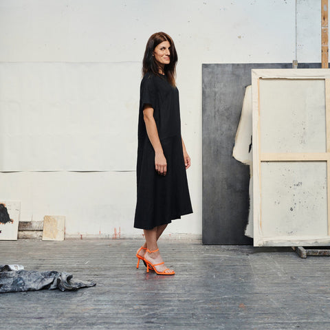 1. Woman wearing black linen A-line dress with orange heels in an art studio setting