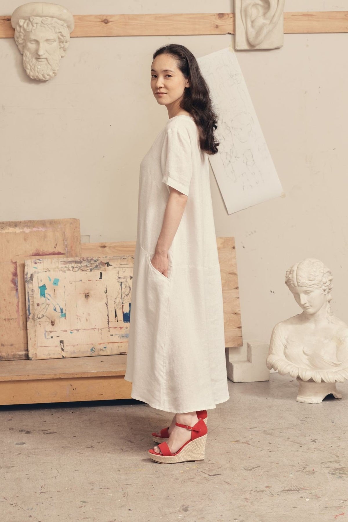 4. Side view of woman in optical white linen dress with red sandals, highlighting A-line fit and pocket detail