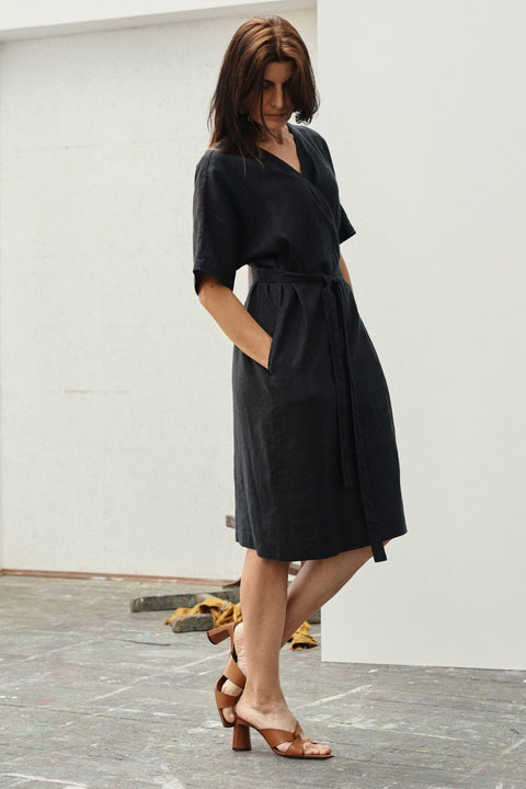 3. Woman in black linen wrap dress with hands in pockets, showing side view in an art studio