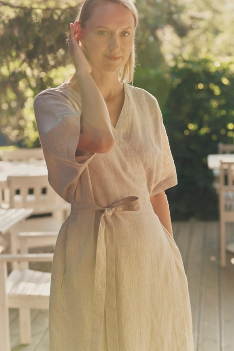 3. Close-up of woman in beige linen wrap dress with V-neck and tied waist, standing on a sunlit deck