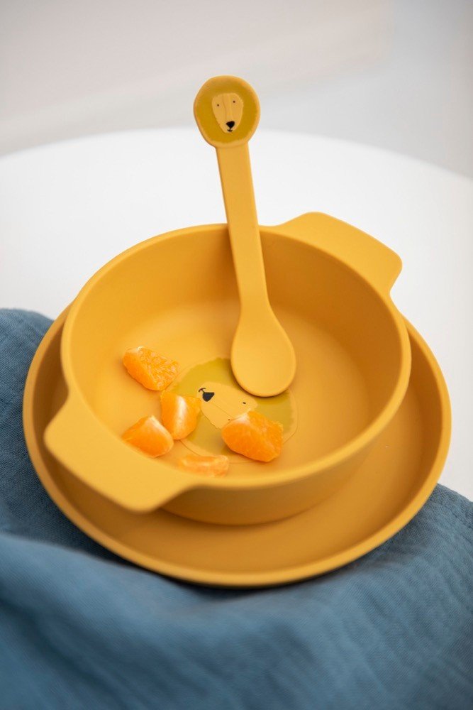 1. Yellow silicone bowl with lion face design and matching spoon on blue cloth, featuring orange slices inside