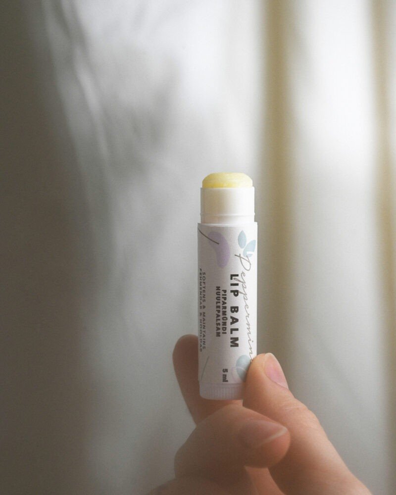 3. Hand holding BONOBO peppermint lip balm with cap off, showing creamy balm, in soft natural lighting